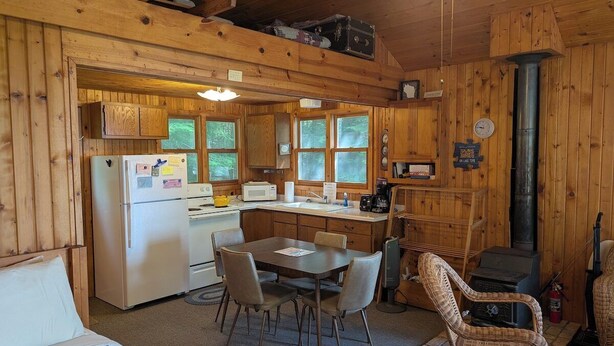 A cabin interior with a dining area, kitchen, and a fireplace. - Simple Gifts - A Simple Studio Cabin with Lake Sup (La Pointe)