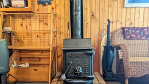 A wood-burning stove with a 'FISHER' brand name, a ladder, and a woven chair in a room with wooden walls. - Simple Gifts - A Simple Studio Cabin with Lake Sup (La Pointe)