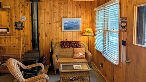 A cozy cabin interior with a wooden interior, a sofa, a chair, a lamp, a fireplace, and a window with blinds. - Simple Gifts - A Simple Studio Cabin with Lake Sup (La Pointe)