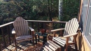 Una terraza de madera con dos sillas Adirondack y una pequeña mesa.