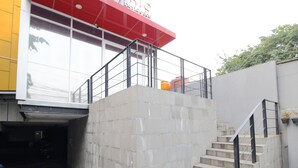 Un edificio con fachada roja y blanca, entrada de vidrio y una escalera de hormigón que lleva a un balcón.