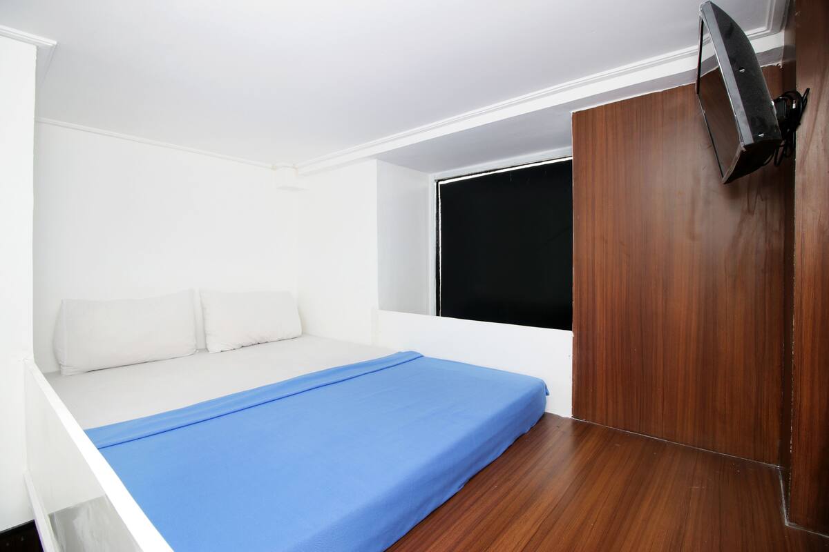 Un dormitorio con una cama, un televisor montado en la pared y una ventana.