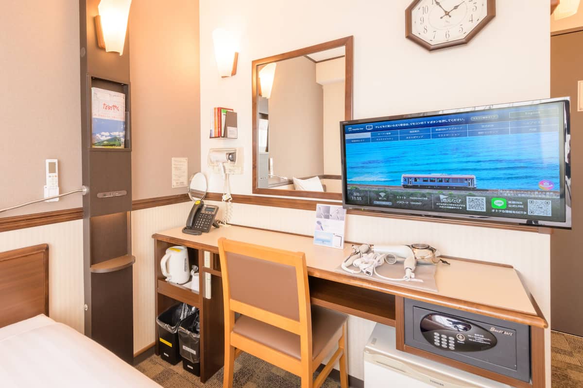 Una habitación de hotel con escritorio, silla, cama y televisión mostrando un tren.