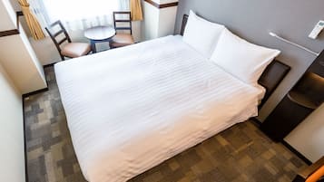 A hotel room with a large bed, a small table, two chairs, and a bedside table with a lamp.
