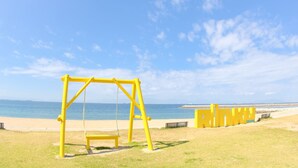 A yellow swing set on a grassy area near a beach with a clear sky. - Toyoko Inn Chubu International Airport No.2 (Tokoname)