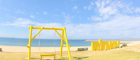 Um baloiço amarelo numa área gramada perto de uma praia, com céu limpo.