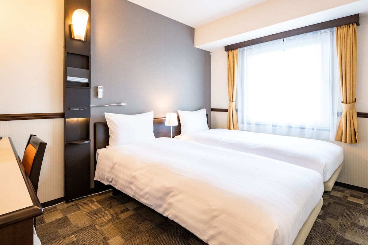 Habitación de hotel con dos camas, un escritorio con lámpara, teléfono y ventana con cortinas.