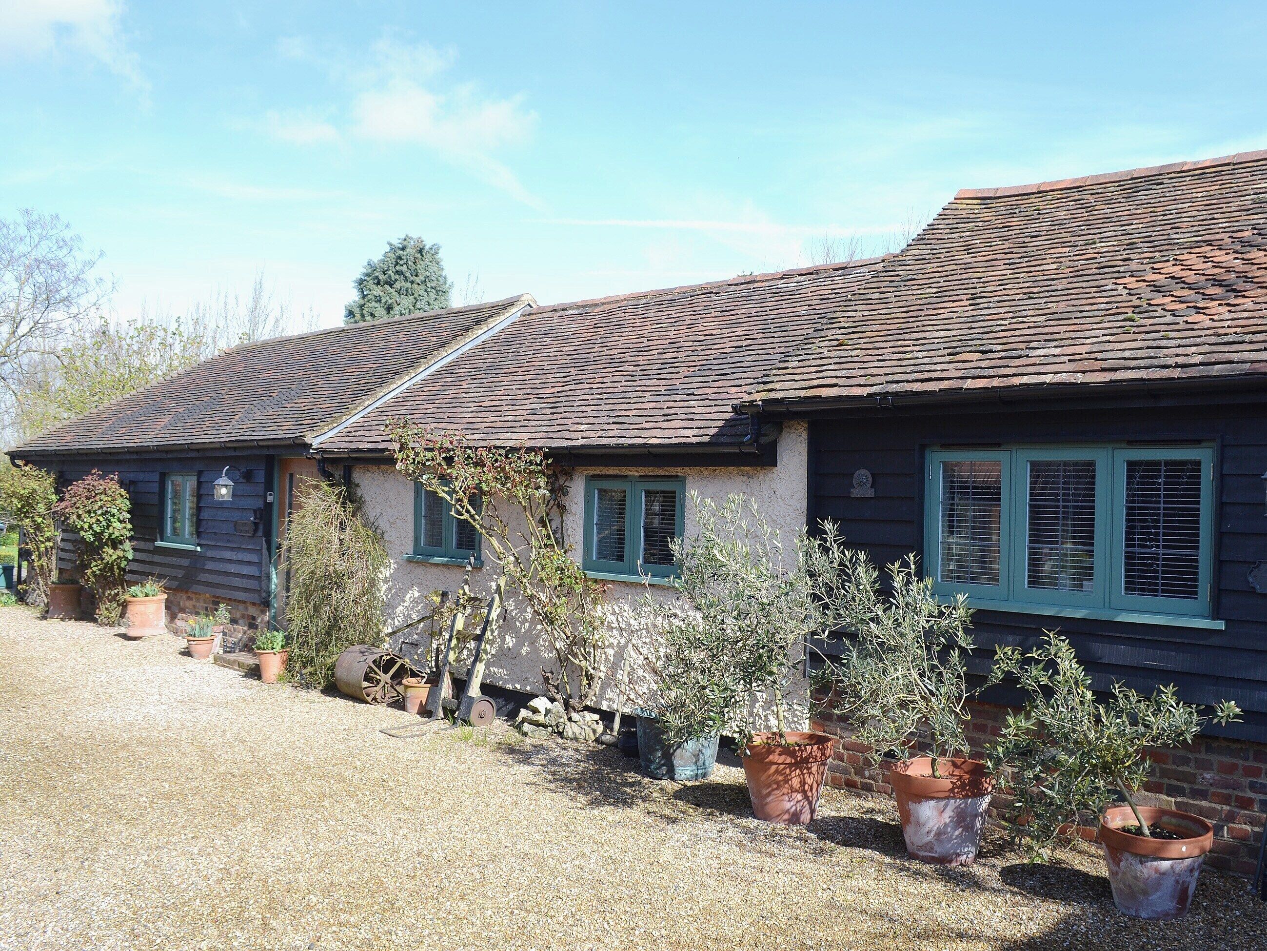 Une maison de campagne traditionnelle avec un toit en tuiles, de nombreuses fenêtres équipées de volets et des plantes en pot dans le jardin.