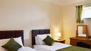 A hotel room with two beds, a nightstand, a lamp, a mirror, and a window with curtains.