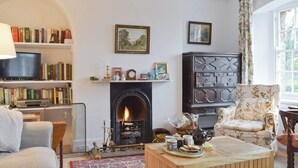 A cozy living room with a fireplace, bookshelves, a television, and a floral armchair. - 3 bedroom accommodation in Church Enstone, near Chipping Norton (Church Enstone, near Chipping Norton)