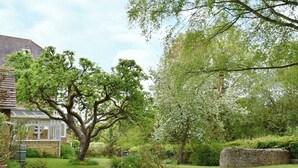 A garden with a large tree, a stone wall, and a house with a white porch. - 3 bedroom accommodation in Church Enstone, near Chipping Norton (Church Enstone, near Chipping Norton)