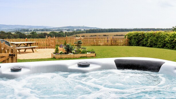 Un jacuzzi con cubierta de madera y vista a un campo cubierto de hierba y colinas.
