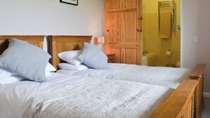Cama doble con cabecera de madera, dos almohadas y una colcha blanca. En la pared hay cuadros enmarcados y un armario de madera.