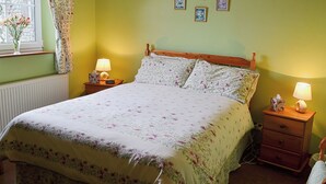 Een slaapkamer met een bloemenprint bedspreider, een houten hoofdbord, nachtkastjes met lampen, en een raam met gordijnen.