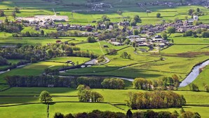 Een landelijk dorpje met een mix van woon- en landbouwgebouwen, een kronkelende rivier en groene velden.