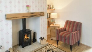 Ein gemütliches Wohnzimmer mit Kamin, einem gestreiften Sessel, einem Bücherregal und einer Lampe.
