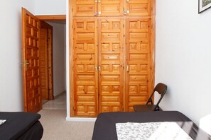 A bedroom with two beds, a wooden wardrobe, and a chair.