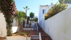 A narrow, tiled pathway leading up a set of stairs between white walls, with greenery and a palm tree on the left. - Cerros del Águila - charming townhouse (Mijas Costa)