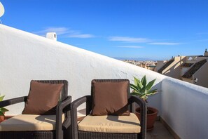 Two wicker chairs with cushions on an outdoor balcony with a view of a cityscape.