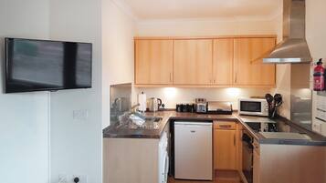 A compact kitchen with wooden cabinets, a microwave, a toaster, and a small refrigerator.