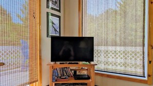 Una habitación con televisión sobre un soporte de madera, una ventana con vistas y una estantería con libros y un reproductor de DVD.