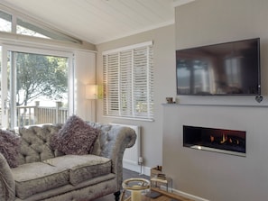 A living room with a sofa, fireplace, TV, and large windows.