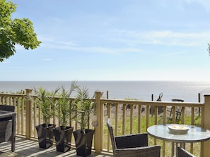 A deck with wicker furniture, potted plants, and a view of the ocean.