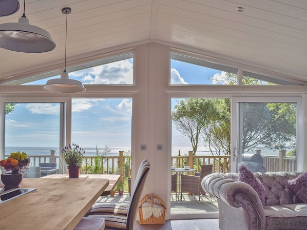 Una habitación amplia con una gran mesa de madera, un rincón de estar con cojines y ventanas que ofrecen vistas al océano.