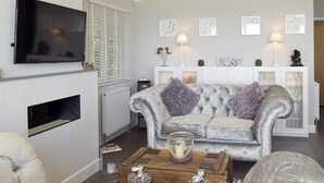 A living room with a sofa, a coffee table, a fireplace, and wall-mounted artwork. - 2 bedroom accommodation in Corton, near Lowestoft (Corton, near Lowestoft)