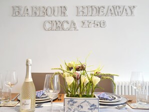 Una mesa de comedor dispuesta con platos, copas, una botella de Freixenet Prosecco y un centro de mesa floral.