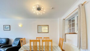 A dining area with a table set for four, wooden chairs, a ceiling light fixture, a wall-mounted mirror, and a window with curtains.