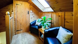 A cozy room with wooden walls, a sloped ceiling, a skylight, a blue leather sofa, a small table, and a potted plant.