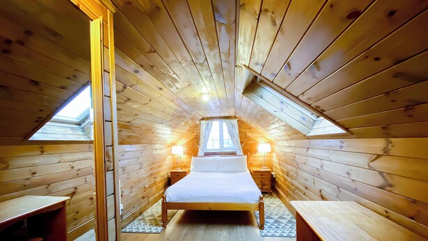 A cozy attic bedroom with a wooden sloped ceiling, a central bed, two bedside tables, and a skylight.