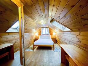 Een gezellig slaapkamer op zolder met een houten schuine dak, een centraal geplaatst bed, twee nachtkastjes en een dakraam.