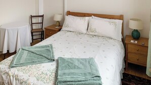 A neatly made bed with floral bedding, two bedside tables with lamps, a chair, and a small table with a lamp. - 1 bedroom accommodation in Ventnor (Ventnor)