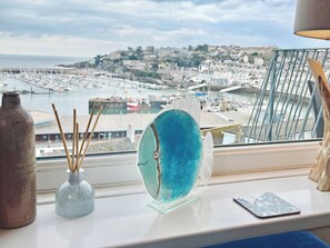 Vista de un puerto con barcos, una obra de arte de vidrio y una botella rústica en un alféizar.