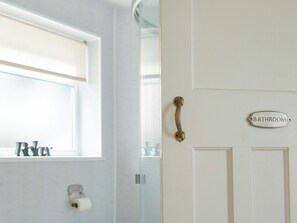 A bathroom with a toilet paper holder, a window with a 'Relax' sign, and a door with a 'Bathroom' sign.