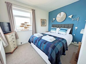 A bedroom with a bed, a television on a dresser, a window with curtains, and wall decor.