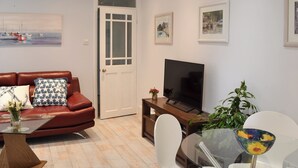 Una sala de estar con sofá de cuero, una mesa de centro de vidrio, un televisor de pantalla plana, una mesa de comedor con sillas y una planta en maceta.