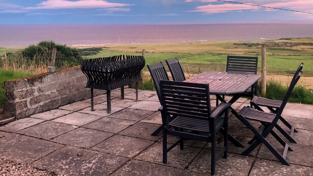 A patio with a table and chairs overlooking a coastal landscape. - 3 bedroom accommodation in Lothmore, Helmsdale (Lothmore, Helmsdale)