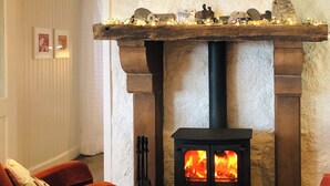 A cozy room with a stone fireplace, a black wood-burning stove, and two red armchairs. - 3 bedroom accommodation in Lothmore, Helmsdale (Lothmore, Helmsdale)