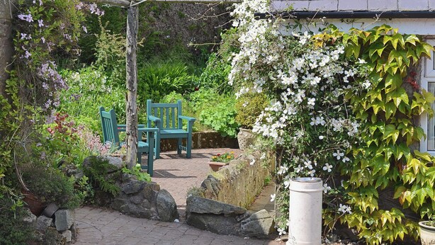 Un jardín con un pérgola, dos sillas verdes y un cubo de basura blanco.