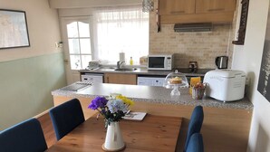Una cocina con comedor, que incluye una mesa de madera, sillas, un jarrón con flores y electrodomésticos como un microondas y una cafetera.