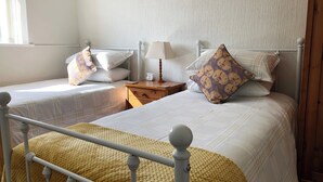 Una habitación con dos camas individuales, una mesita de noche de madera con una lámpara y una ventana con cortinas.