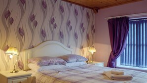 Una camera da letto con un letto, due comodini, una lampada da comodino, una finestra con tende e carta da parati decorata.