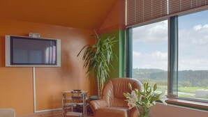Un soggiorno con una poltrona in pelle, un tavolino in vetro, una TV a parete e una grande finestra con vista sulla campagna.