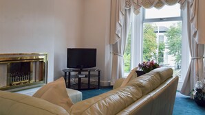 A living room with a leather sofa, a television on a stand, and a fireplace. - 2 bedroom accommodation in Southport (Southport)