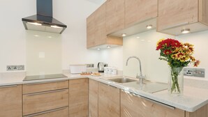 A modern kitchen with wooden cabinets, a stainless steel sink, and a built-in range hood. - The Old Meeting Hall (King&rsquo;s Somborne, near Winchester)