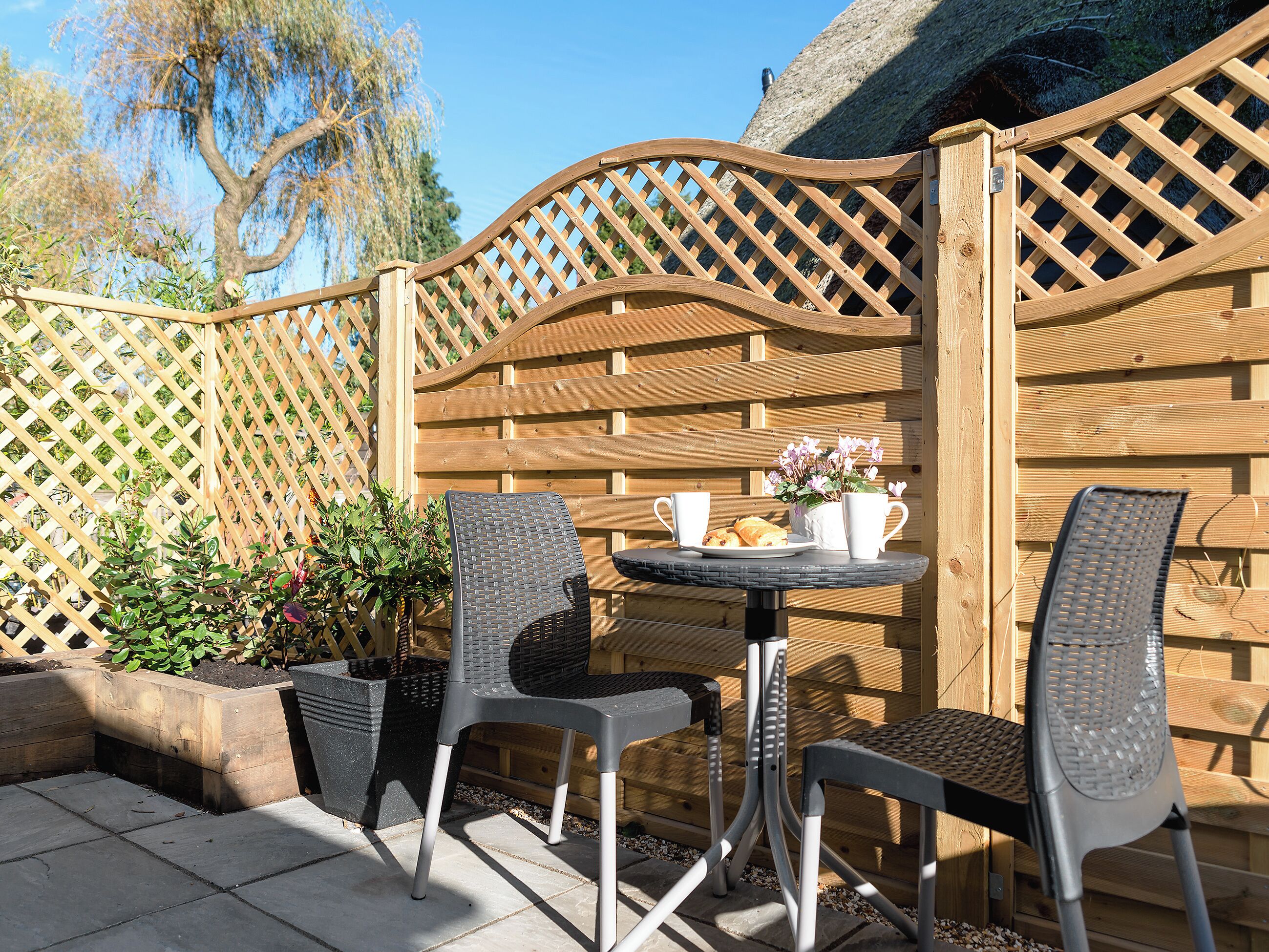 A patio with two chairs, a table, and a wooden fence.