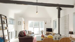 A modern living room with a sofa, dining table, chairs, a TV, and a fireplace. - The Old Meeting Hall (King&rsquo;s Somborne, near Winchester)